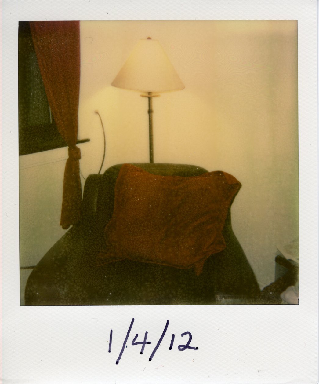 An arm chair with a lamp behind it. There is a large red pillow on the chair.