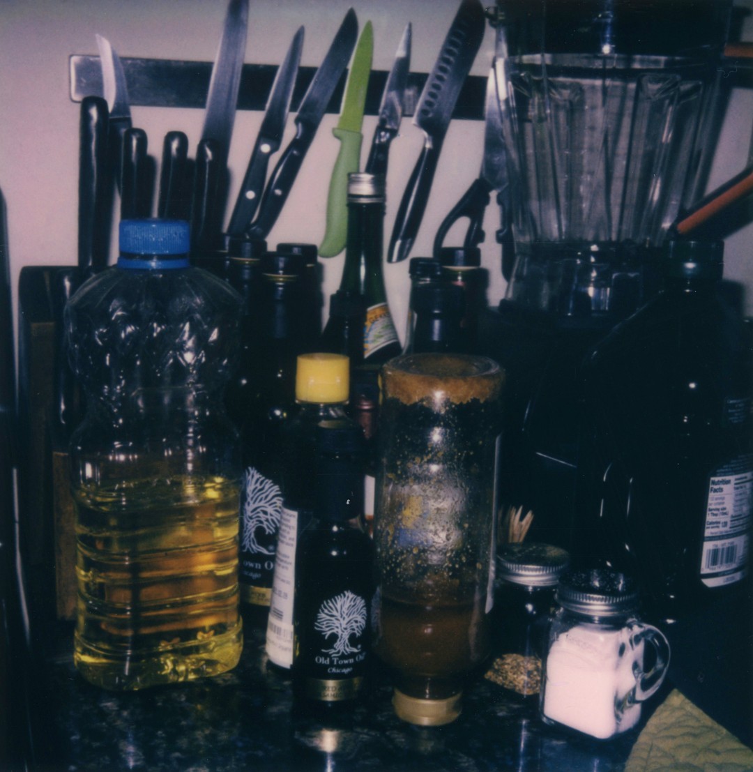 A cluttered countertop featuring olive oils, spices and honey.