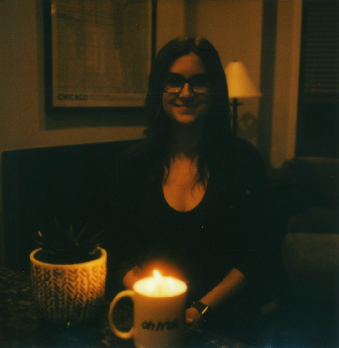 A woman sitting in a kitchen with a mug cake in front of her with a candle lit.