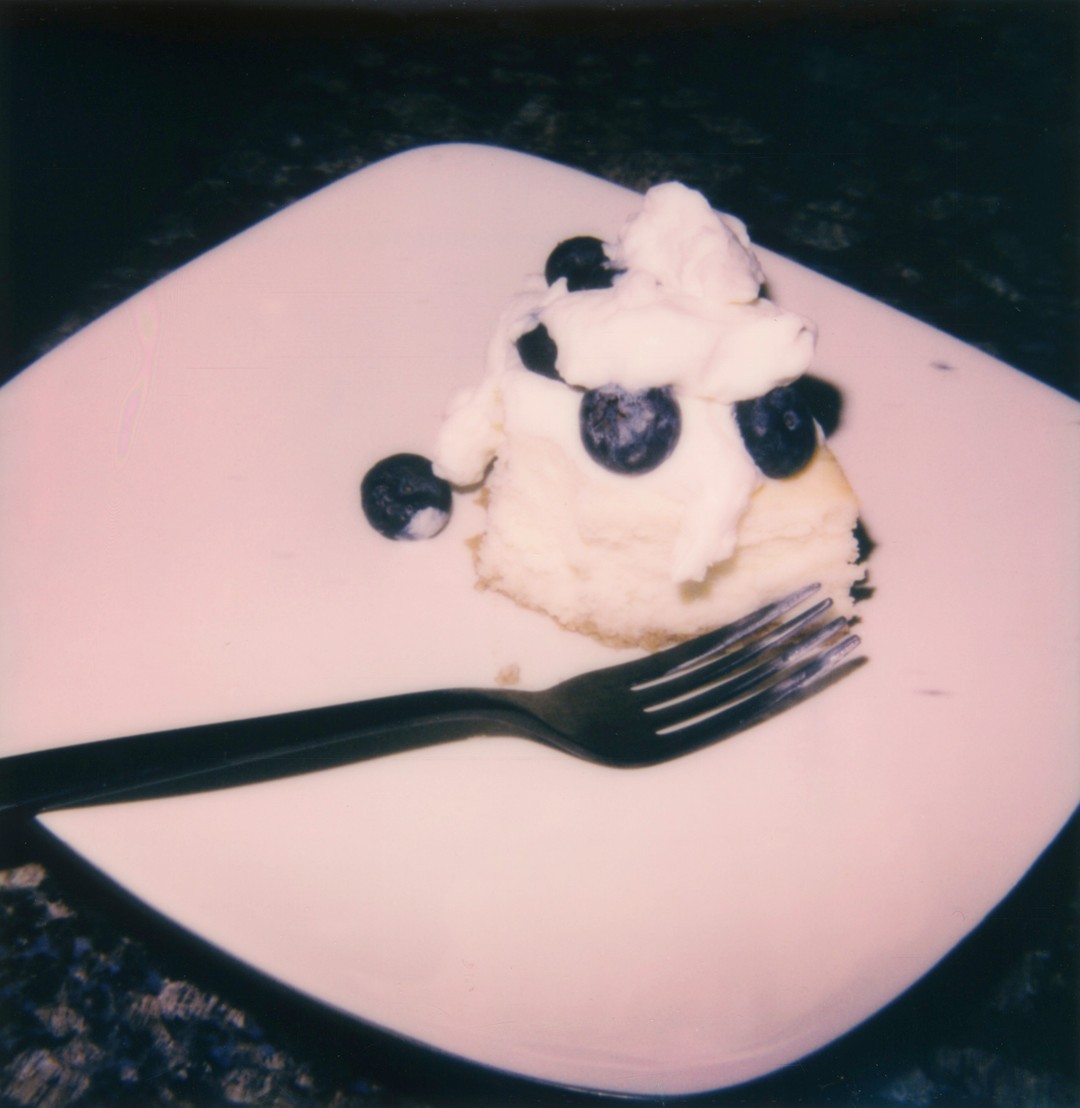 A piece of blueberry cheesecake on a white rectangular plate with a black fork.