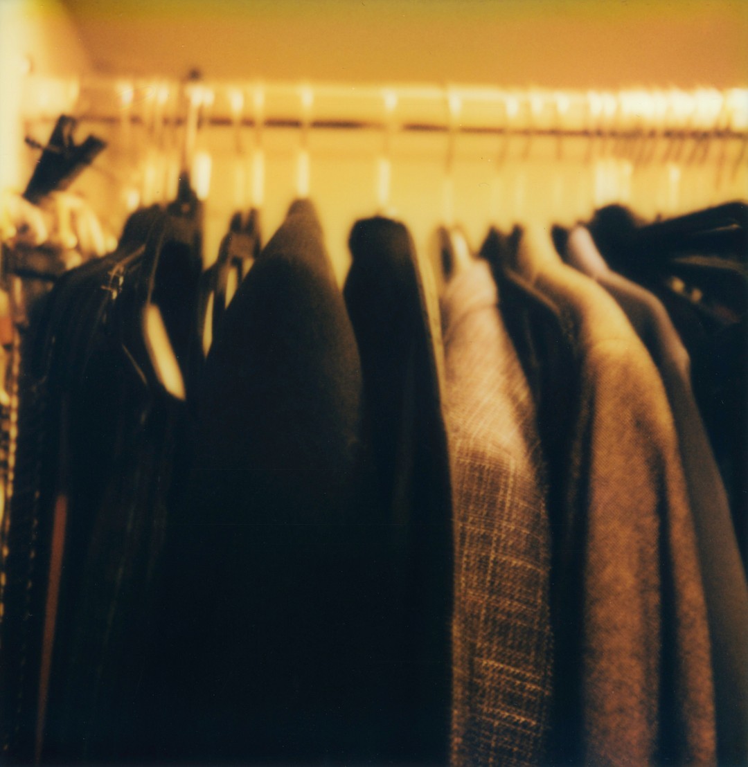 A photograph of the inside of a man's closet filled with suit jackets.